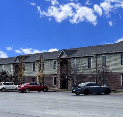 A red car is parked in front of a building with a stone pillar.