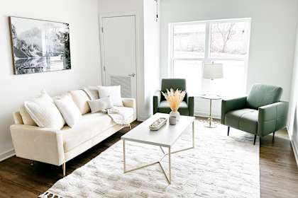 A white couch with a white coffee table in front of a white wall with a black and white picture hanging on it.