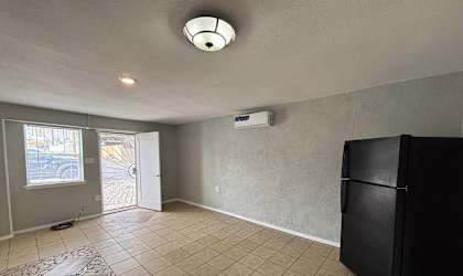 A black refrigerator sits in a room with a tiled floor and a window.