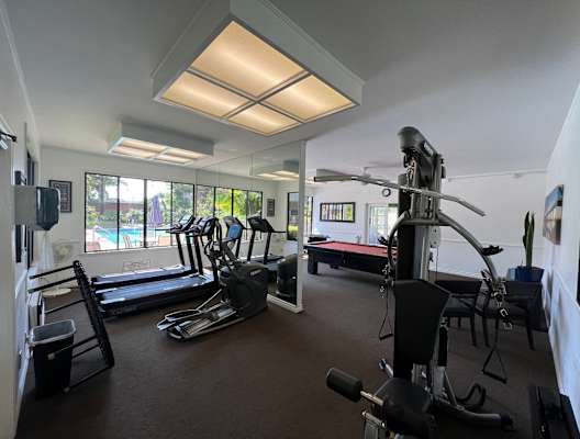 a gym with exercise equipment and windows with a pool