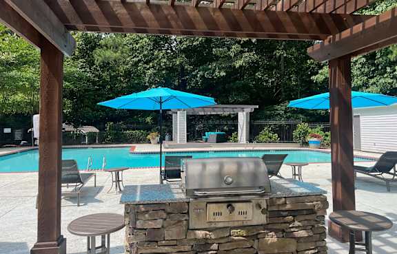 a pergola with a grill and umbrellas overlooking a swimming pool