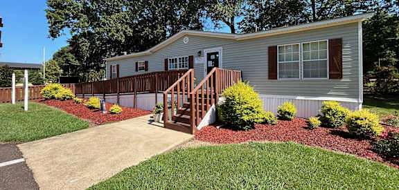 A house with a grey siding and a red door is surrounded by a garden with red mulch.
