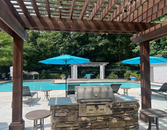 a pergola with a grill and umbrellas overlooking a swimming pool