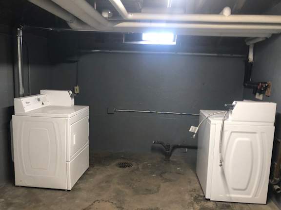 Two white washing machines in a basement.