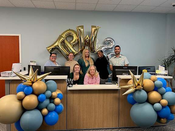 a group of people standing behind a desk with balloons
