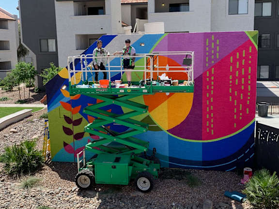 Two people painting a mural on a wall.