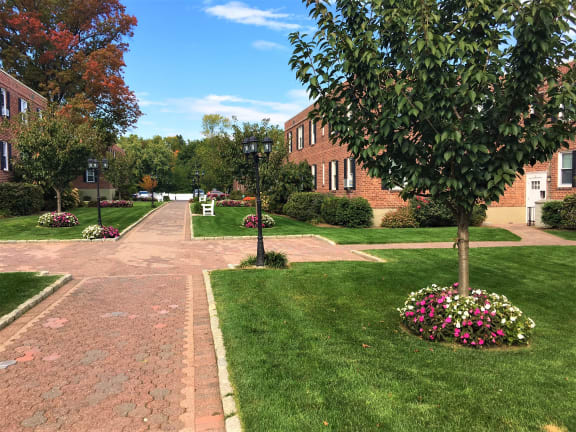 a walkway in front of a brick building with trees and flowers