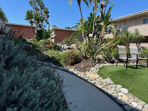 a garden with a walkway and chairs in front of a building