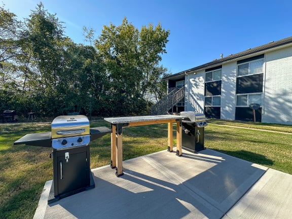 a picnic table and two gas grills in front of a house