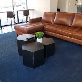 A brown leather couch sits in a blue rug in a room with a desk and chairs.