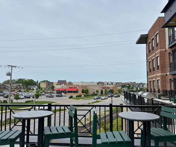 A patio with green chairs and tables overlooks a parking lot and buildings.