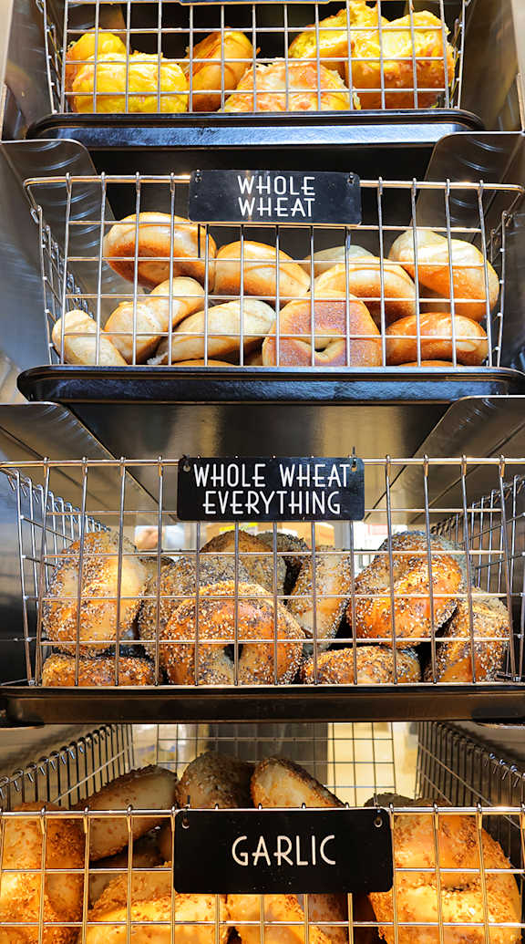 A display of breads with labels for whole wheat, sesame, poppy, everything, and garlic. at Trio Newton Apartments, Newton, MA, 02460