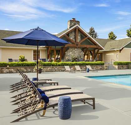 A pool with sun loungers and a blue umbrella in front of a house.