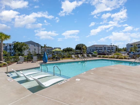 a pool and lounge chairs in a yard with apartments in the background