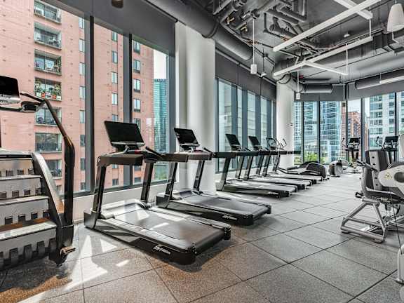 a row of treadmills in a fitness room with a view of the city