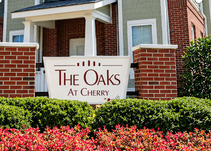 A sign that says The Oaks at Cherry in front of a building.