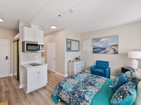 A bedroom with a blue bed and a painting on the wall. at Legacy Hills at Poway 55+ Apartments, Poway, California