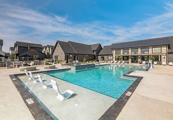 A large swimming pool with a diving board in the foreground and houses in the background.