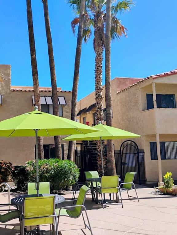 A pool area with a green umbrella and chairs.
