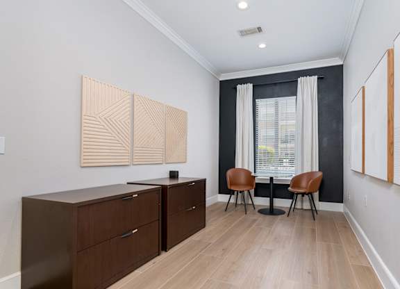 A room with a brown cabinet, two chairs and a table.