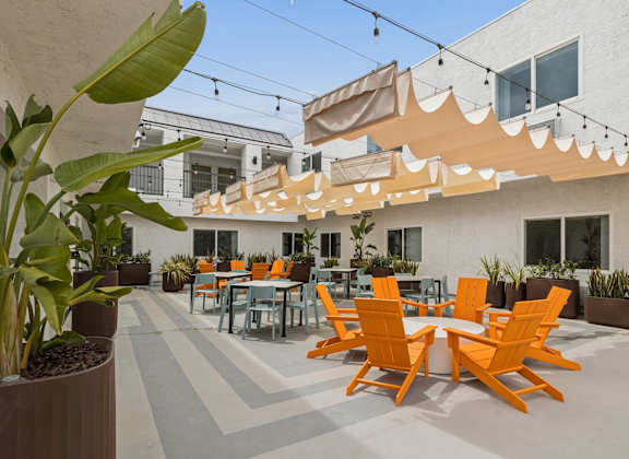 A patio with orange chairs and a white building in the background.