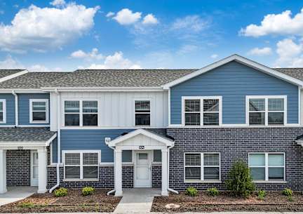 A blue and white townhouse with a front yard and a driveway.at Hawthorne Pointe, Bondurant, IA
