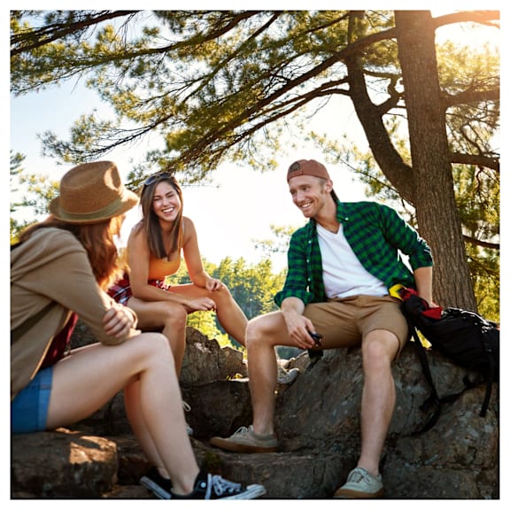 Three friends sitting on a rock in a forest.