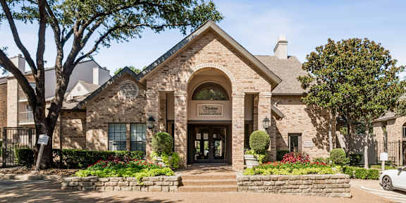 A building with a stone facade and a sign that reads "Ladies' Manor" is surrounded by trees and flowers.