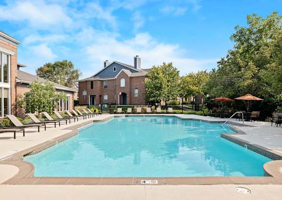 A large swimming pool surrounded by lounge chairs and trees.