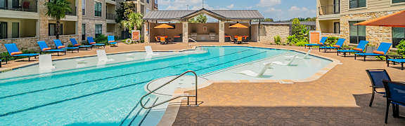 A large swimming pool surrounded by a stone patio and lounge chairs.
