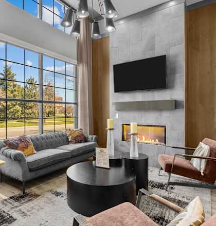 A modern living room with a grey couch, a fireplace, and a large window.