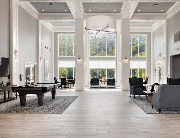 A large, open-concept living room with a pool table and a view of the trees outside the windows.