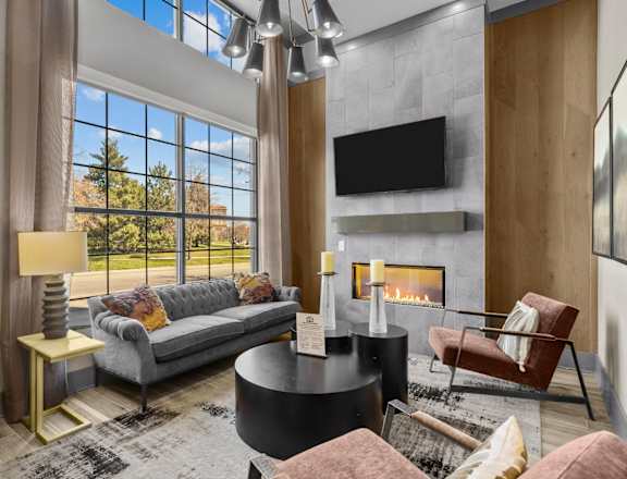 A modern living room with a grey couch, a fireplace, and a large window.
