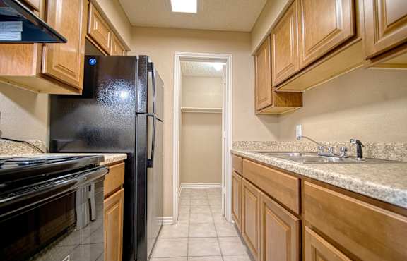A kitchen with a black refrigerator and wooden cabinets.