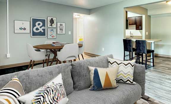 A grey couch with striped pillows sits in a room with a dining table and chairs.