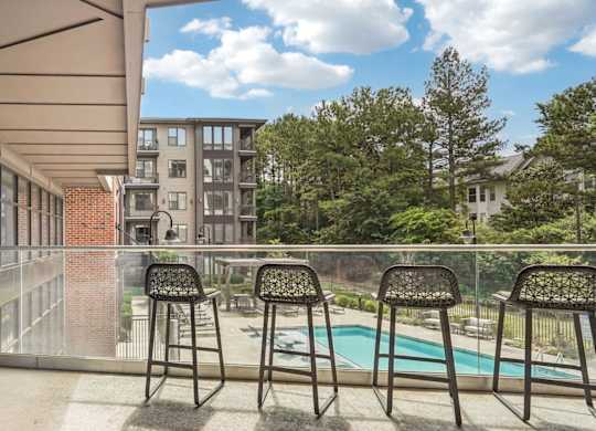 A patio with chairs and a swing overlooking a pool.