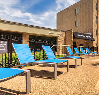 Pool deck with blue lounge chairs and apartment buildings at Harvard Square Apartments in Dallas