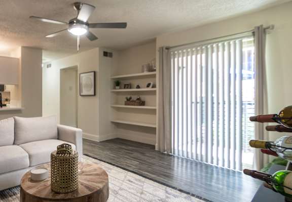 Living room view in a 1-bedroom apartment at Cambridge Court Apartments in Dallas, Texas, showing staged seating, wood-style flooring, patio door, and connection to the kitchen.
