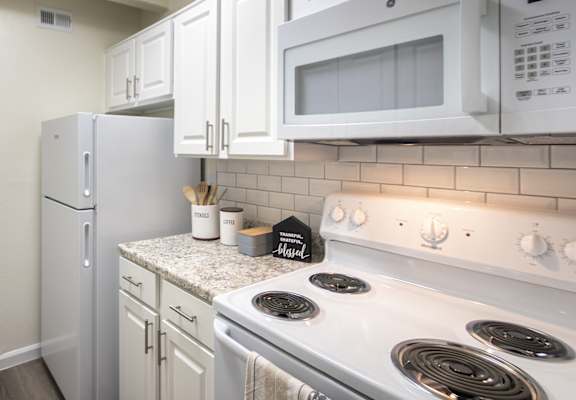 Galley kitchen with white cabinets and full-size refrigerator in a one-bedroom apartment home at Harvard Square Apartments