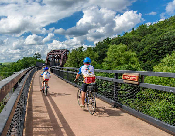 two people riding bikes on a bridge over a river