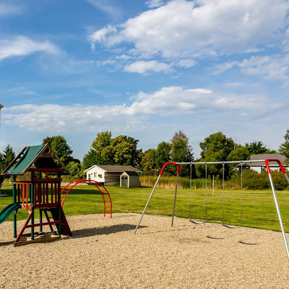 A playground with a green slide and a red swing set in front of a building.