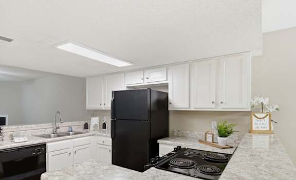 A kitchen with a black fridge, white cabinets, and a marble countertop.