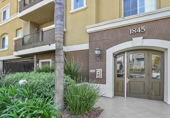 the entrance to an apartment building with a sidewalk and plants