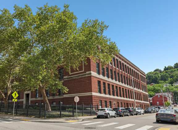 A street view with a red brick building, cars, and trees.