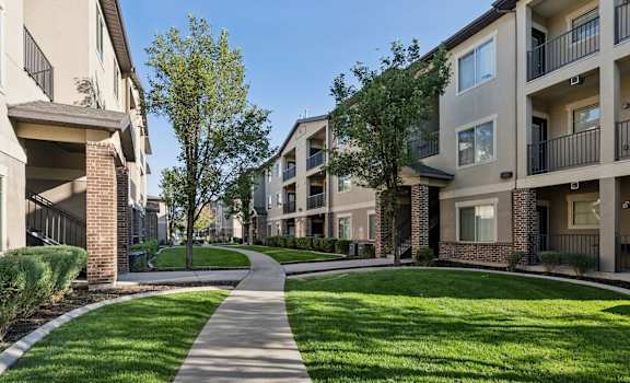 a walkway between two apartment buildings with grass and trees