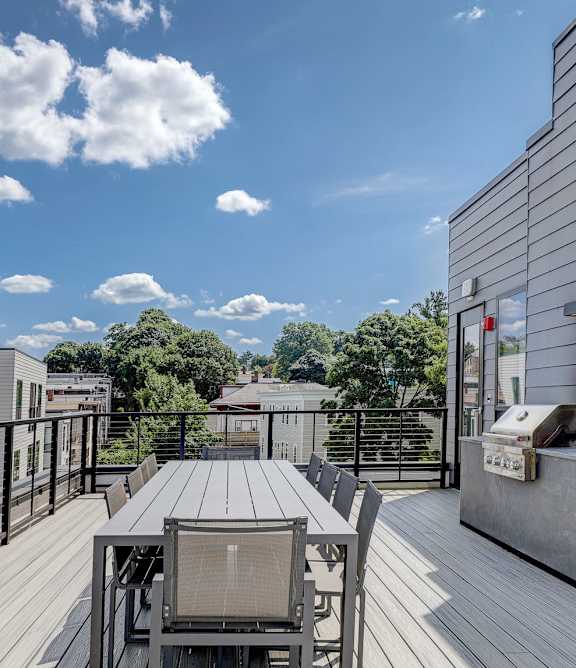 A wooden deck with a table and chairs overlooking a cityscape at sunset.