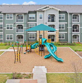 A playground area with a slide and swings in front of apartment buildings.
