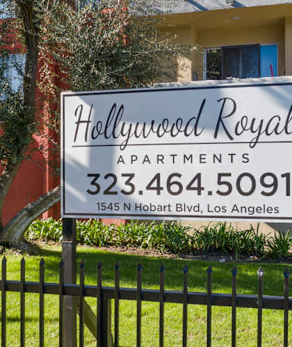 A sign for Hollywood Royale Apartments stands in front of a building.
