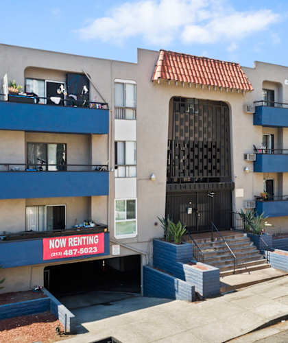 A building with a sign that says "Now Renting" is in front of a car.