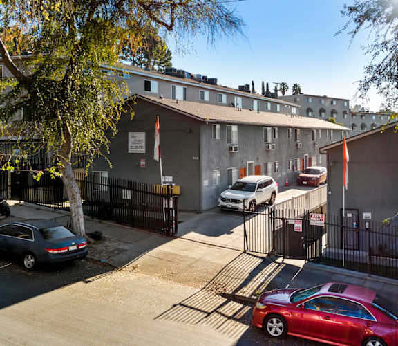 A red car is parked in front of a building with a black fence.